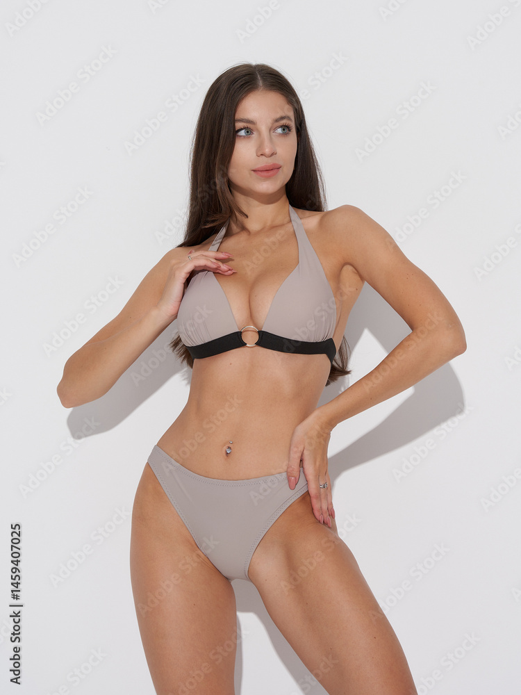 A woman stands confidently wearing a two-piece swimsuit, featuring a halter top with a ring detail, against a plain setting. She has long hair and is accessorized with a silver ring A woman stands confidently wearing a two-piece swimsuit, featuring a halter top with a ring detail, against a plain setting. She has long hair and is accessorized with a silver ring