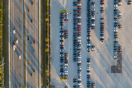 Aerial view of dealership parking lot with many brand new cars for sale near wide american highway. Development of US automotive industry concept