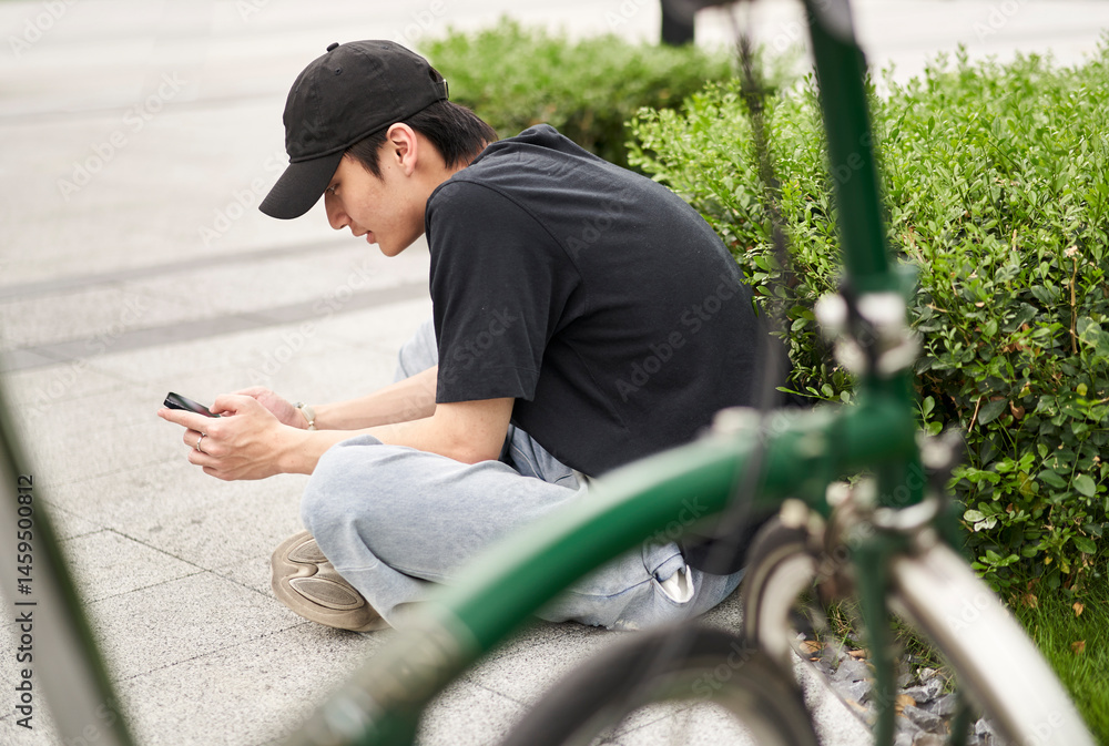 Obraz premium handsome young Asian man sitting on ground beside his bike smiling