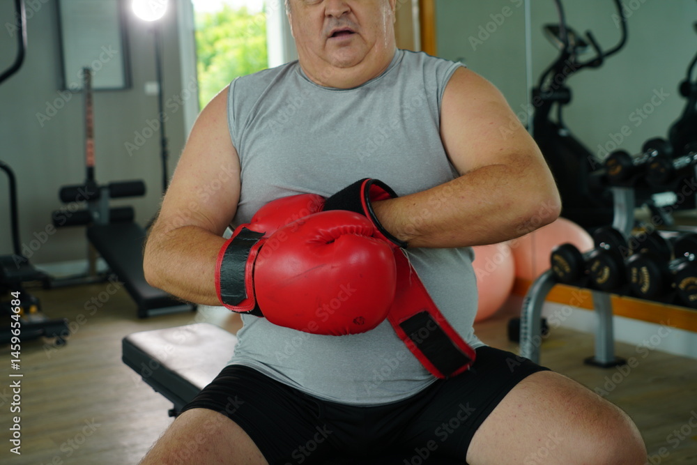 Elderly Caucasian man with a fat belly wearing gym clothes wearing red gloves practicing boxing and punching doing exercises for health and lose weight in a fitness centere.