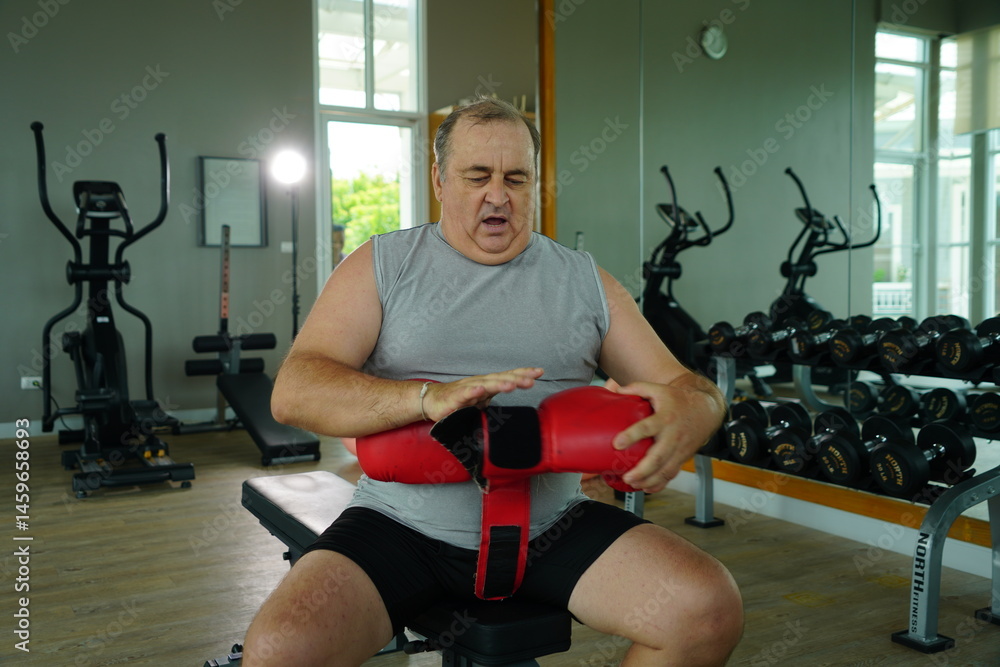 Elderly Caucasian man with a fat belly wearing gym clothes wearing red gloves practicing boxing and punching doing exercises for health and lose weight in a fitness centere.