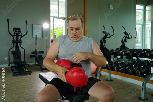Elderly Caucasian man with a fat belly wearing gym clothes wearing red gloves practicing boxing and punching doing exercises for health and lose weight in a fitness centere.