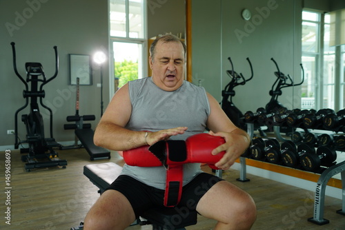 Obraz na płótnie Elderly Caucasian man with a fat belly wearing gym clothes wearing red gloves practicing boxing and punching doing exercises for health and lose weight in a fitness centere. w salonie