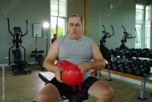 Obraz na płótnie Elderly Caucasian man with a fat belly wearing gym clothes wearing red gloves practicing boxing and punching doing exercises for health and lose weight in a fitness centere. w salonie