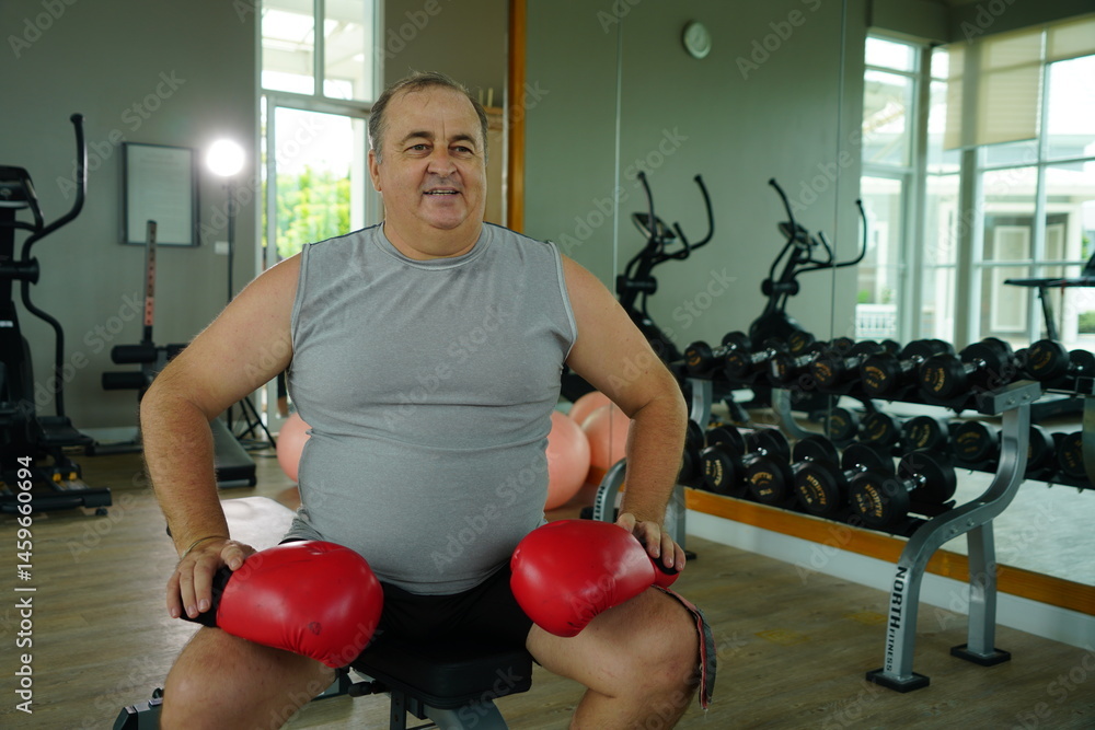 Elderly Caucasian man with a fat belly wearing gym clothes wearing red gloves practicing boxing and punching doing exercises for health and lose weight in a fitness centere.