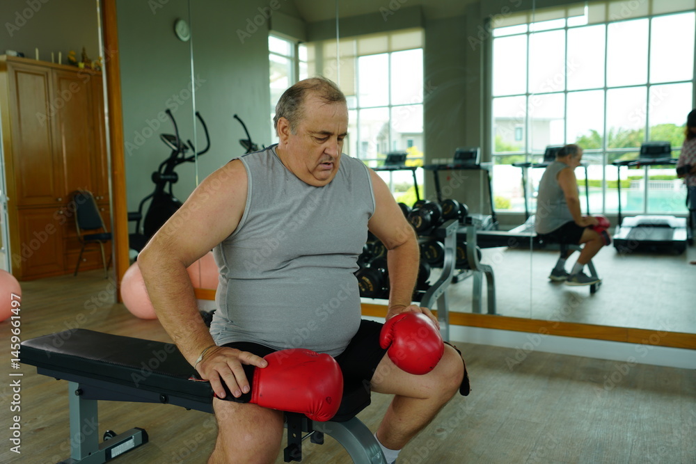 Elderly Caucasian man with a fat belly wearing gym clothes wearing red gloves practicing boxing and punching doing exercises for health and lose weight in a fitness centere.