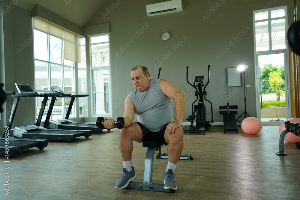 Elderly Caucasian man with a fat belly wearing gym clothes lifting dumbbells doing exercises to build muscle for health and lose weight in a fitness center Health and wellness concept
