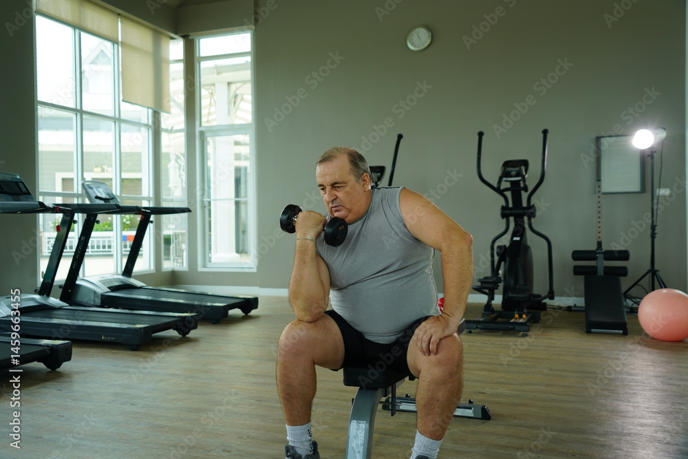 Elderly Caucasian man with a fat belly wearing gym clothes lifting dumbbells doing exercises to build muscle for health and lose weight in a fitness center Health and wellness concept