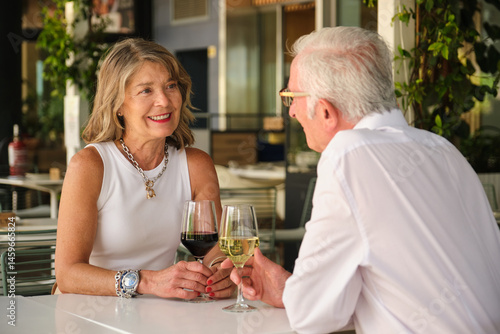 Obraz na płótnie Happy retired couple drinking wine at an outdoor restaurant, enjoying a romantic moment together w salonie