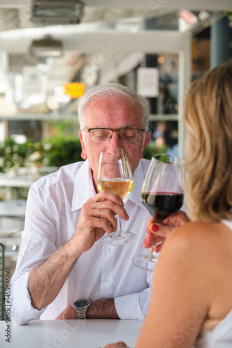 Obraz na płótnie Senior man smelling a glass of white wine with closed eyes, a woman is drinking red wine next to him w salonie