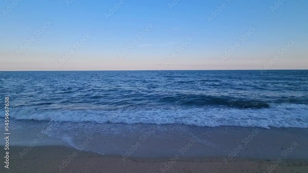 Evening sea waves crashing onto sandy shore under blue evening sky. Coastal seascape and ocean motion background. Summer travel and marine nature concept. Evening sea waves crashing onto sandy shore under blue evening sky. Coastal seascape and ocean motion background. Summer travel and marine nature concept.