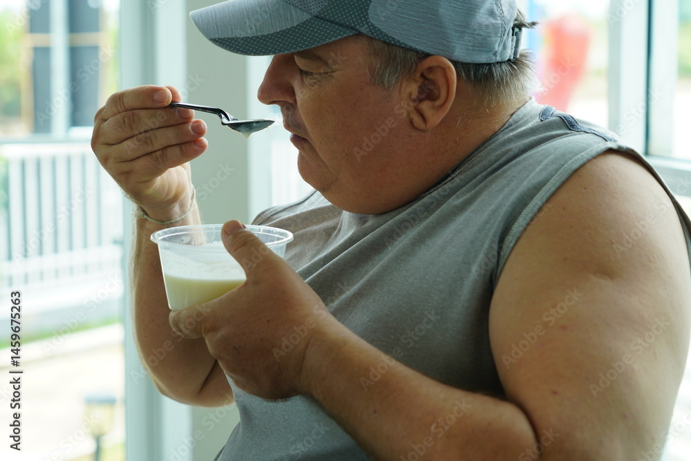 Fat Caucasian senior man with potbelly after workout hungry eating breakfast yoghurt,fruit salad healthy food and weight loss in fitness club. Health and wellness concept.