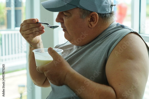 Fat Caucasian senior man with potbelly after workout hungry eating breakfast yoghurt,fruit salad healthy food and weight loss in fitness club. Health and wellness concept.