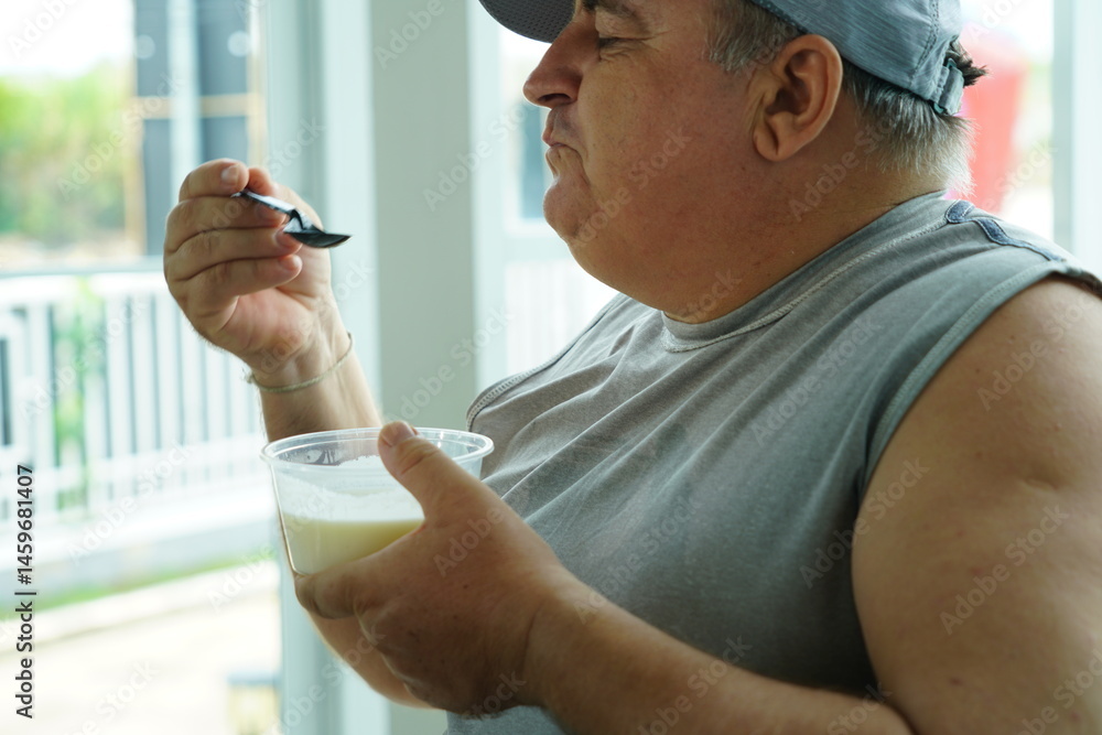 Fat Caucasian senior man with potbelly after workout hungry eating breakfast yoghurt,fruit salad healthy food and weight loss in fitness club. Health and wellness concept.