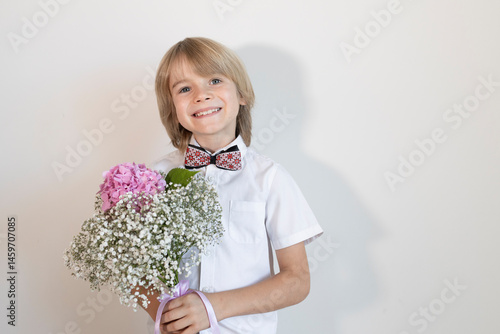 portrait of sincere little happy smiling 7-8 year old blond boy with flower bouquet on light background. young gentleman. gift for mother's day, birthday. Copy space