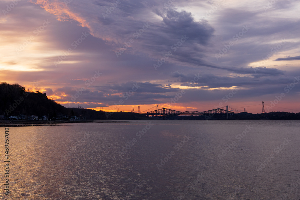 Panorama of the Pierre-Laporte and Quebec bridges in silhouette against a dramatic purple sunrise over the St. Lawrence River, Cap-Rouge area, Quebec City, Quebec, Canada Panorama of the Pierre-Laporte and Quebec bridges in silhouette against a dramatic purple sunrise over the St. Lawrence River, Cap-Rouge area, Quebec City, Quebec, Canada