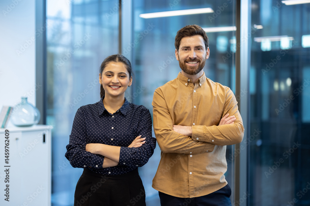 Smiling business professionals stand together with arms crossed in a bright, modern office setting, ready for success.
