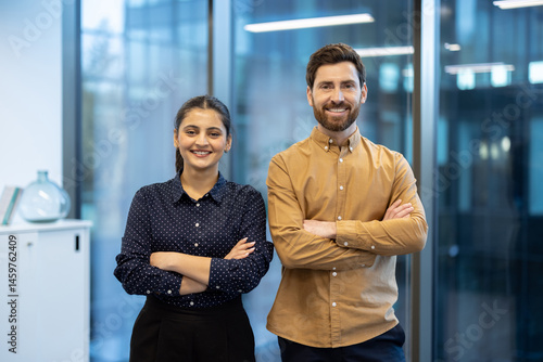 Obraz na płótnie Smiling business professionals stand together with arms crossed in a bright, modern office setting, ready for success. w salonie