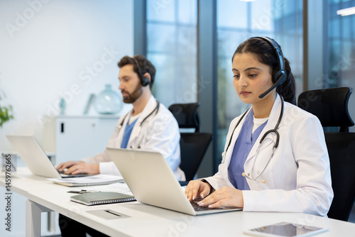 Obraz na płótnie Two doctors are seen in an office setting, wearing headsets and using laptops. They may be providing remote medical consultations. w salonie