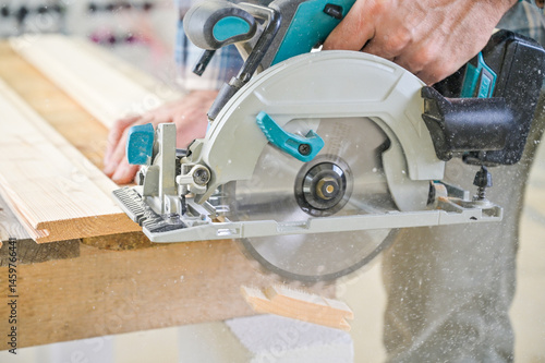 Obraz na płótnie A skilled craftsman operates a circular saw on a wooden plank, showcasing precision and craftsmanship in a well-lit workshop environment, highlighting woodworking techniques w salonie