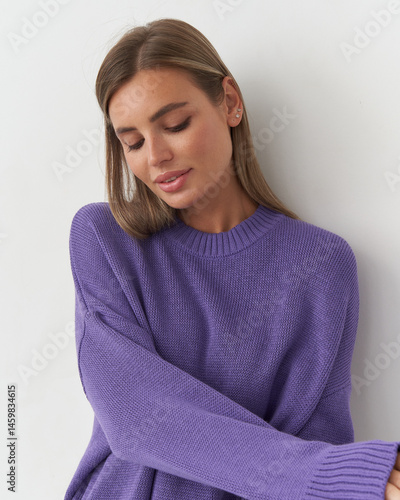 Captivating female model in stylish purple sweater poses elegantly in studio setting