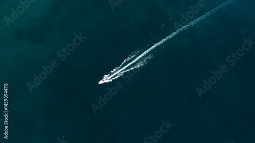 Obraz na płótnie Aerial zenithal view of a motorboat crossing the blue sea. Its passage leaves a white trail on the surface of the water. w salonie