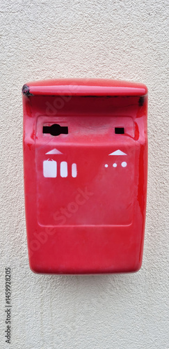 Obraz na płótnie A bright red, slightly weathered metal box with white symbols is mounted on a textured light-colored wall, indicating a collection point for old batteries w salonie