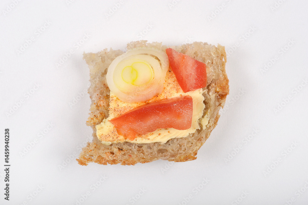 A piece of bread topped with vegan butter, tomato, and onion rings is presented on a plain white surface