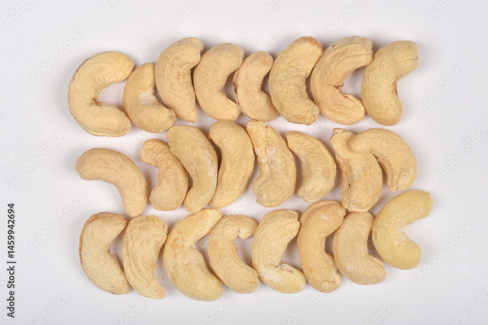 Three horizontal rows of raw cashew nuts are neatly arranged on a light gray surface