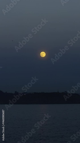 Full moon rising over dark coastal landscape at night