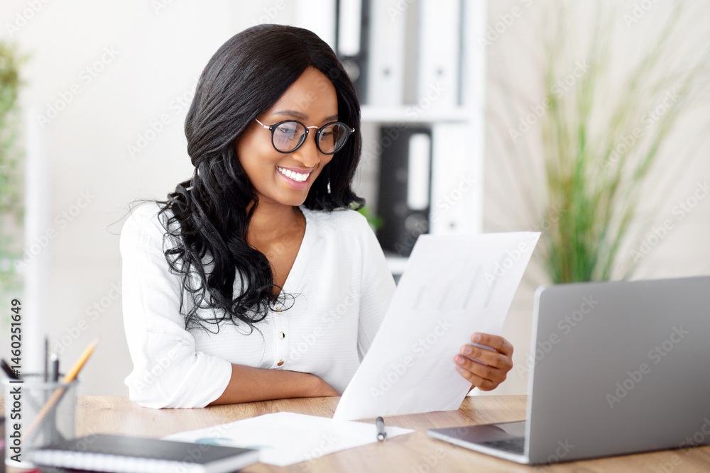 Attractive black businesswoman working with documents in front of laptop in modern office. African American female secretary looking trough contract or agreement at workplace Attractive black businesswoman working with documents in front of laptop in modern office. African American female secretary looking trough contract or agreement at workplace