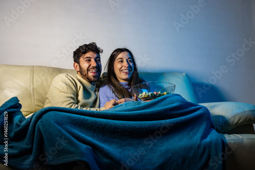 Happy couple watching tv and eating popcorn on sofa at night