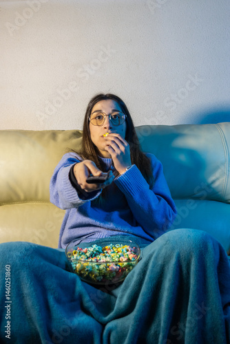 Young woman watching tv and eating popcorn on sofa at night