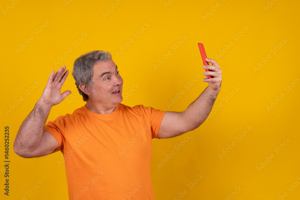 Enthusiastic senior man taking a selfie with smartphone on yellow background Enthusiastic senior man taking a selfie with smartphone on yellow background