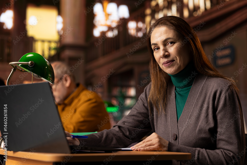 Mature woman at a college campus study area writing notes and ideas, focused on her academic graduation preparation at the library. Female student learning for personal development.