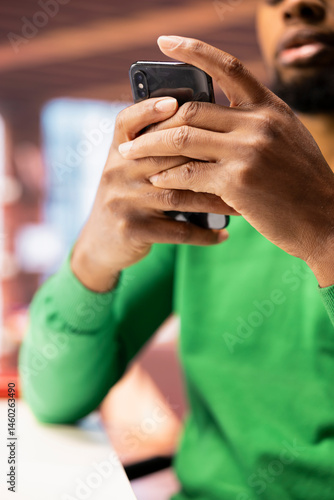 Obraz na płótnie Man in home office using smartphone to compose social media posts, producing content. Close up of african american person monitoring social media engagement using mobile phone w salonie
