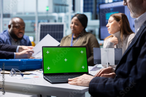 Shareholders and production plant manager analyzing sustainable manufacturing data using green screen laptop. Investors review documentation on chroma key notebook to evaluate investment profitability