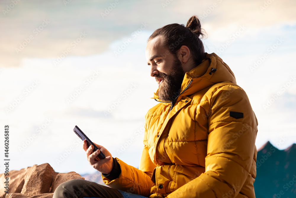 Nature lover relaxing on mountain top getting online with his phone at a scenic viewpoint, looking out over the landscape. Hiker staying always online and connected, panoramic scenery.