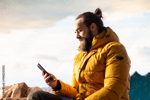 Obraz na płótnie Nature lover relaxing on mountain top getting online with his phone at a scenic viewpoint, looking out over the landscape. Hiker staying always online and connected, panoramic scenery. w salonie