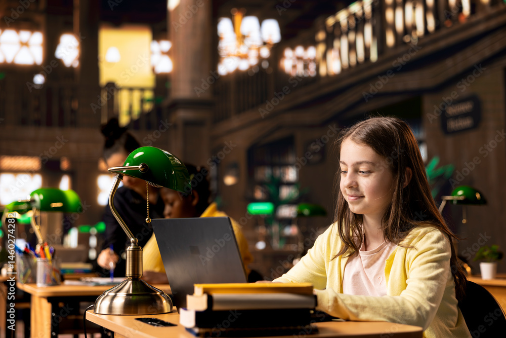 Preteen student writing a digital essay during productive homework session in a library, highlighting preparation for a class lesson. Focused girl working on her laptop to get good grades.