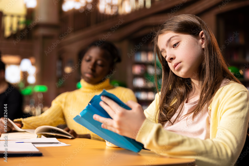 Preteen students focus on reading the required books at a study desk, developing their academic skills and literary language at the library. Scholars enjoying lecture for the school curriculum.