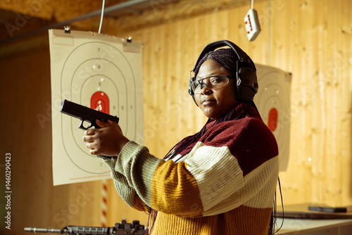 Obraz na płótnie Portrait of shooting gallery customer doing training, learning proper pistol holding etiquette. African american woman practicing with handgun, wearing safety equipment to prevent injury w salonie
