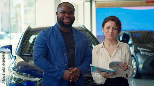 Obraz na płótnie Portrait of happy customers in car showroom browsing automobiles catalog, checking characteristics and features before taking test drive. Cheerful clients comparing vehicle models, camera A w salonie
