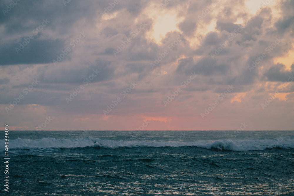 Fototapeta premium view of the ocean with waves just before a sunrise with colorful clouds