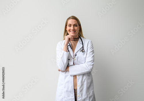 Bilde på lerret Portrait of smiling young female doctor in lab coat and with hand on chin standi