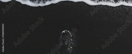 Foot in dark sand as ocean water washes shore in monochrome beach scene, nature?s power on display
