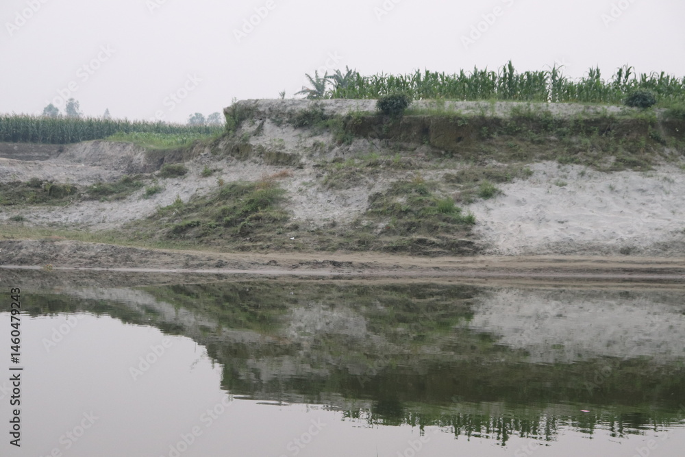 Rural Riverbank View with Earth Cliff, Greenery, and Calm Water Reflection