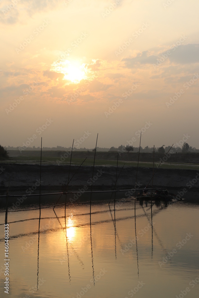 Tranquil water reflection of bamboo bridge with golden sunlit sky at dusk