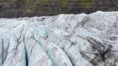 Drone rotating over soothy glacier surface, mossy cliff background, in Iceland photo