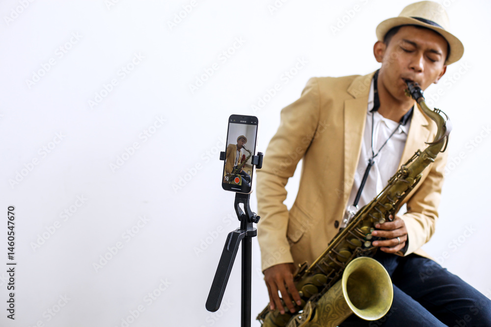 Fototapeta premium Portrait Of Saxophonist Playing A Music While Recording Vlog Using Smartphone At Music Studio